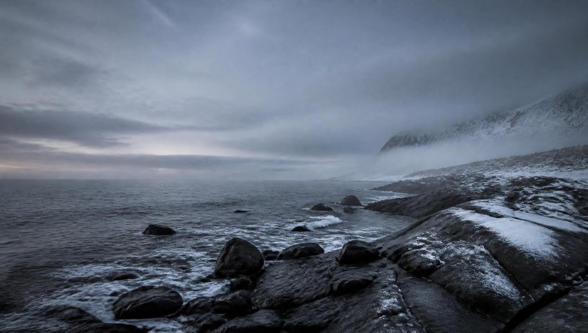 Cold Nordic coastline of dark granite and grey sea under low fog